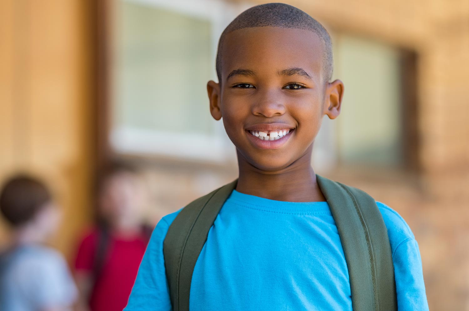 A small boy in a bright, blue shirt smiles widely to show off his white teeth.