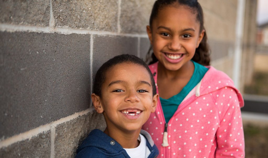 A small boy in a bright, blue shirt smiles widely to show off his white teeth.