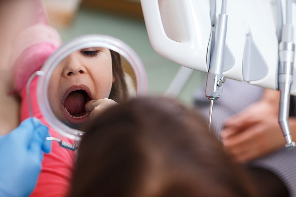 little girl looks at her teeth in a mirror